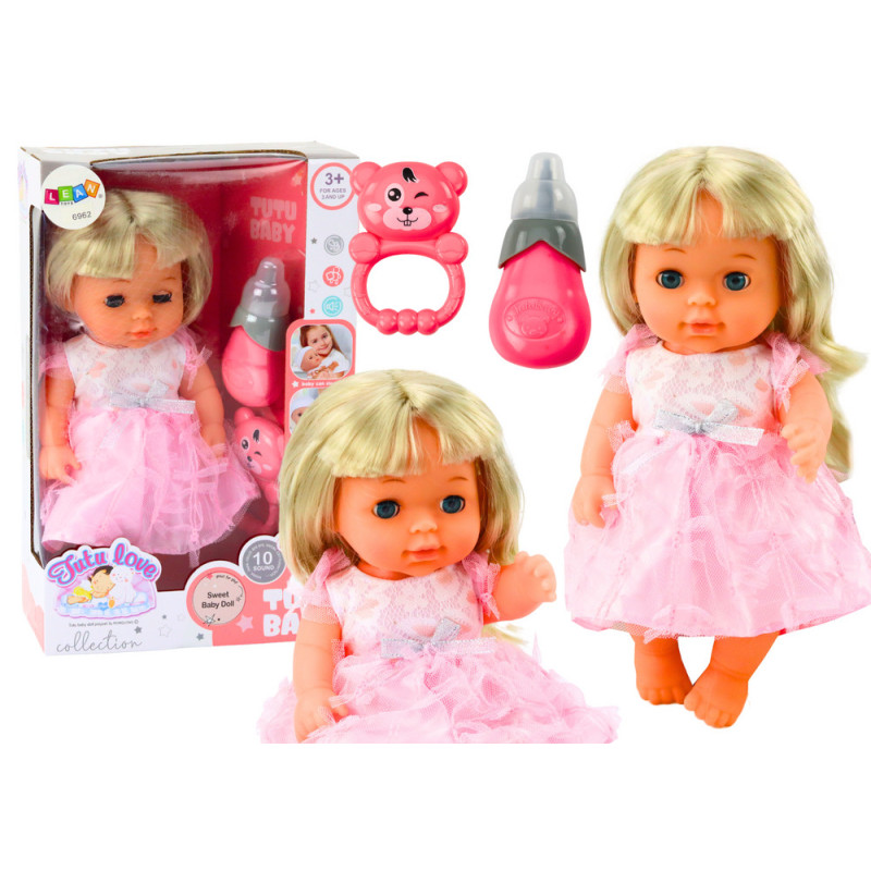 Dockan i en ljusrosa klänning som skakar en skallraflaska ljudligt.